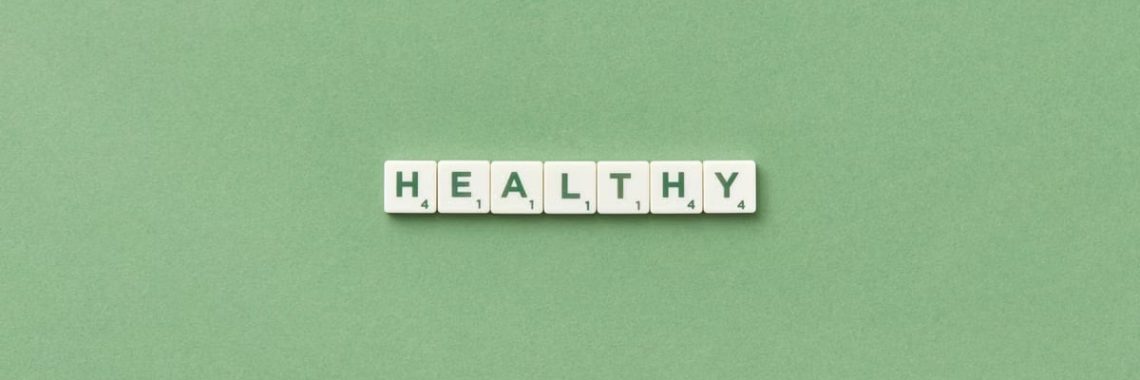 Scrabble tiles spelling the word 'healthy' on a light green background, top view.